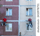 Renovation of the facade of an apartment building by industrial climbers side view. Sealing of seams between plates. The work of steeplejack repair block of the house.