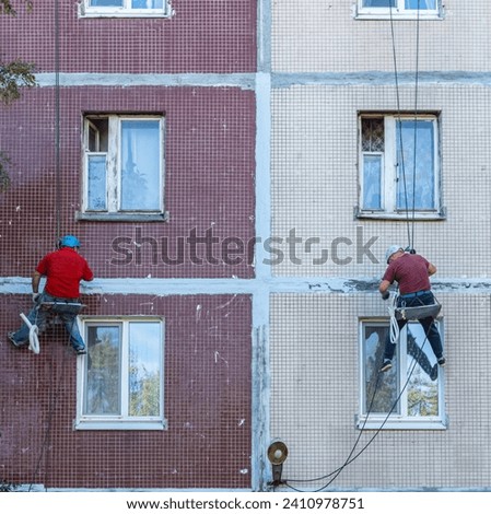 Renovation of the facade of an apartment building by industrial climbers side view. Sealing of seams between plates. The work of steeplejack repair block of the house.