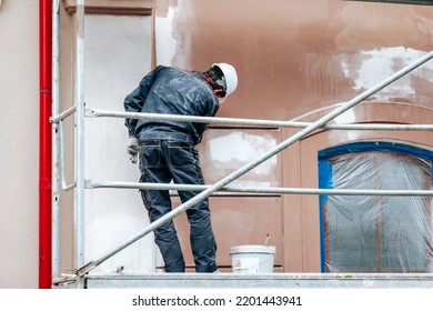 Renovation, restoration, refurbishment. Unrecognizable worker renovating wall of classical style building, standing on scaffolding. Construction worker prepares house facade wall for painting outdoors - Shutterstock ID 2201443941