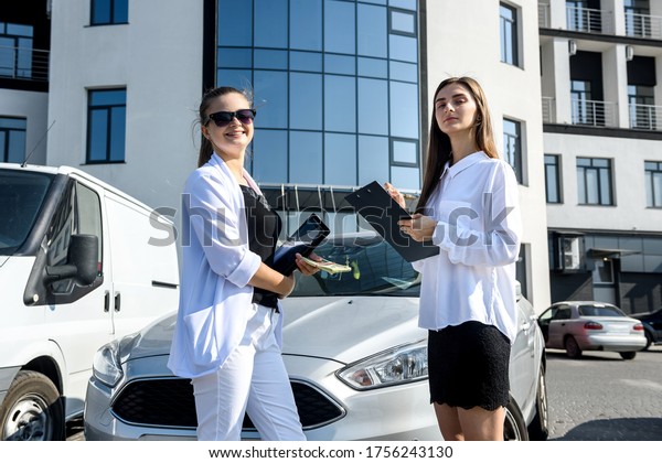 Rent or car buy concept. Two women with dollar bundle\
posing near car