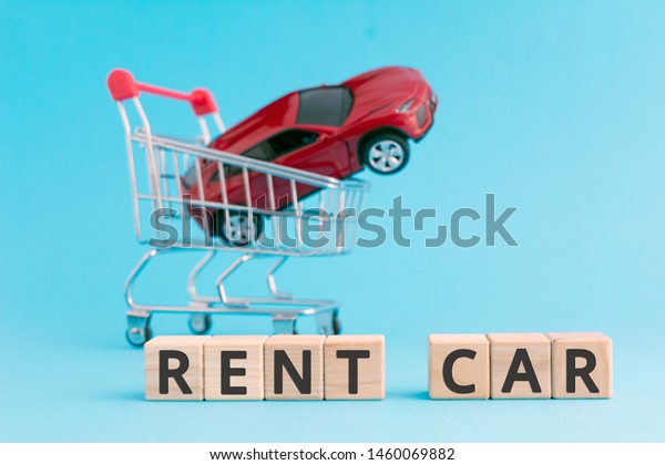 rent car wooden\
cubes letters red toy car in shopping cart, car rental service\
company concept blue\
background