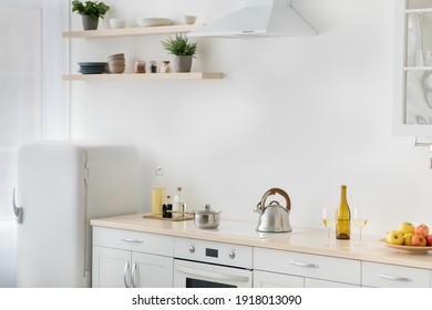 Rent flat, real estate, ready for cooking, domestic culinary, home healthy eat. White kitchen, refrigerator, stove with kettle, plate with apples, shelves with potted plants and utensils, light wall
