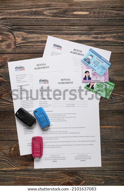 Rental agreements, driver licenses and car\
keys on wooden\
background