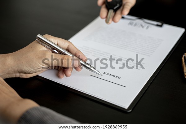 The renter is signing a car rental agreement with\
the car rental company. After discussing the details and charges\
with the employee, the employee hand over the car keys to the\
renter.