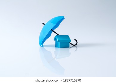 Renters home insurance or mortgage protection concept with a 3D house model under a blue umbrella