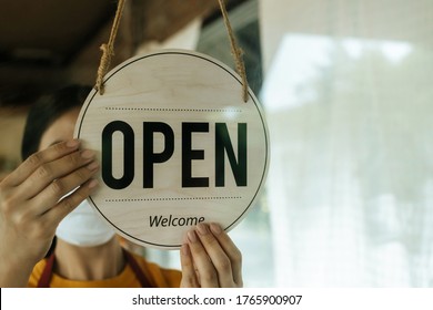 Reopen. waitress woman wearing protection face mask turning "Open" sign board reopen after coronavirus quarantine is over in cafe coffee shop ready to service, cafe restaurant, food and drink concept - Shutterstock ID 1765900907