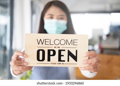 Reopen, Young Asia girl wear face mask turning a sign from closed to open sign after lockdown.  - Shutterstock ID 1933296860
