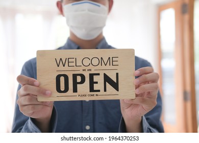 Reopen, Young Asia man wear face mask turning a sign from closed to open sign after lockdown.  - Shutterstock ID 1964370253