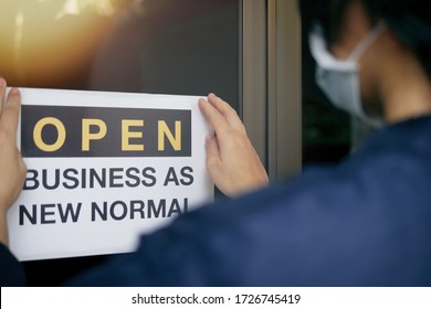 Reopening for business adapt to new normal in the novel Coronavirus COVID-19 pandemic. Rear view of business owner wearing medical mask placing open sign “OPEN BUSINESS AS NEW NORMAL” on front door. - Shutterstock ID 1726745419