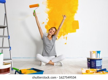 Repair in the apartment. Happy young woman paints the wall with  yellow  paint
 - Powered by Shutterstock