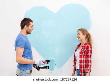 Repair, Building And Home Concept - Smiling Couple Painting Big Heart On Wall At Home