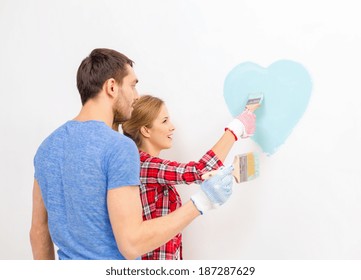 Repair, Building And Home Concept - Smiling Couple Painting Small Heart On Wall At Home