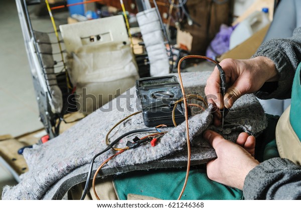 Repair of car seat\
heating. Car mechanic\'s hands is using multimeter to check a\
voltage in cable of\
heating.