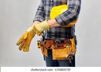 Repair, Construction And Building - Male Worker Or Builder With Helmet And Working Tools On Belt Putting Protective Gloves On Over Grey Background