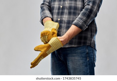 Repair, Construction And Building - Male Worker Or Builder With Putting Protective Gloves On Over Grey Background