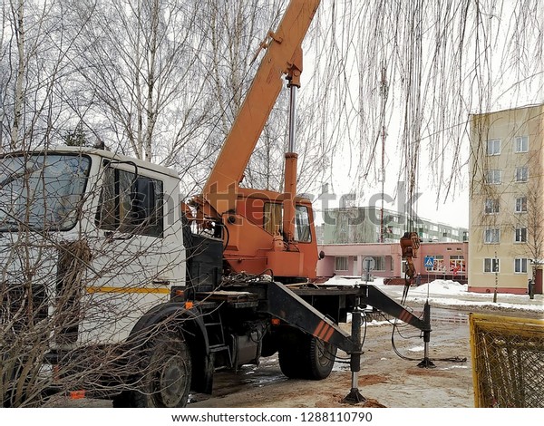 repair construction works, the automobile\
crane with hydraulic telescopic arrow against the background of\
houses, the road, trees, winter, snow, close\
up