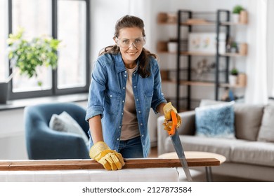 Repair, Diy And Home Improvement Concept - Happy Smiling Woman In Goggles With Saw Sawing Wooden Board