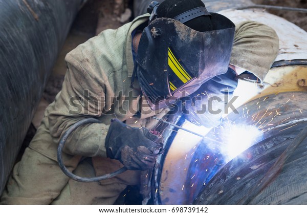 Repair of heating duct. The workers, welders made\
by electric welding and gas welding on large iron pipes at a depth\
of excavated trench.
