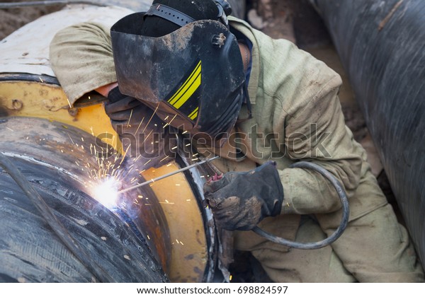 Repair of heating duct. The workers, welders made\
by electric welding and gas welding on large iron pipes at a depth\
of excavated trench.