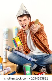 Repair Home Man Holding Paint Roller For Wallpaper. Tired And Frustrated Mad Male In Newspaper Cap Renovation Apartment. Paint Bank And Paint Brush In Hand. Loan For Housing For Students.