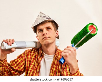 Repair Home Man Holding Paint Roller For Wallpaper. Tired And Frustrated Male In Newspaper Cap Renovation Apartment. Paint Bank And Roll Paper Background On Isolated. Young Student Builder.