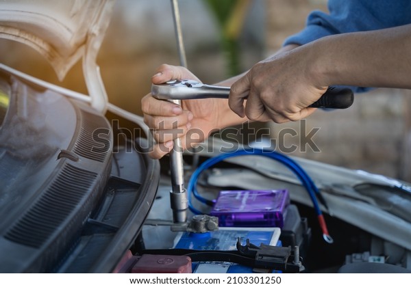 Repair and installation of the battery. The man\
tightens with a wrench bolts for fastening a new battery,\
installing spare parts for a\
car.
