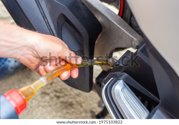 Repair and\
maintenance of a motorcycle. Oil change. The car mechanic pours oil\
into the engine through a rubber\
hose.