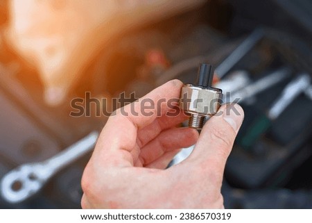 Repair man installing new knock sensor in car. Man repair broken car, engine detonation, change broken knock sensor. Electrician hold in hand new sensor, replacing faulty electric spare part. 