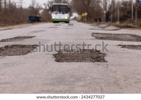 Repair patch in the road and a bus in the background that is moving towards this pothole