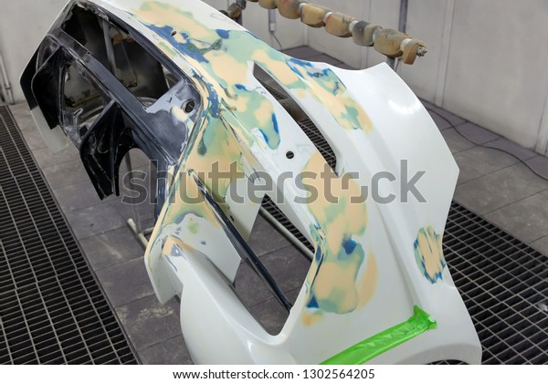 Repair of the rear bumper of a white car\
after an accident with the help of multi-colored putty in a\
workshop for painting vehicles in a special\
chamber