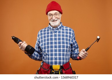 Repair, renovation, construction and occupation concept. Picture of emotional funny unshaven elderly carpenter or plumber going to fix something, laughing happily, holding drill and hammer