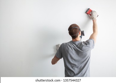 Repair And Renovation At Home. New Interior Design. Worker Scrubbing The Wall With Sandpaper And Prepare The Surface For Painting. Man Using Respirator.