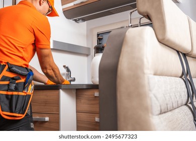 A repair technician in an orange uniform is focused on fixing kitchen fixtures inside a modern RV. The technician appears attentive, using tools to address maintenance issues, showcasing the detailed  - Powered by Shutterstock