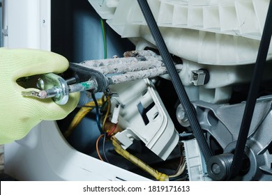 Repair of a washing machine, replacement of heating element affected by scale and limescale, hand in green glove close-up.
