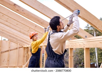 Repair of wooden roof outdoors. Two constructors in special clothes work in new house. Male and female Roofing contractors measuring the the distance between the boards, wearing working uniform - Powered by Shutterstock