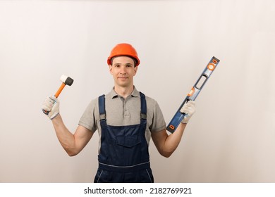 Repair Work And Construction Concept. Repairman In Blue Overalls And Helmet With A Rubber Mallet And A Building Level. Copy Space.