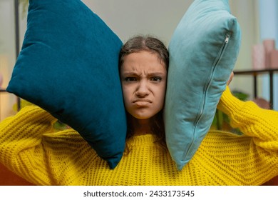 Repair work at neighbors. Irritated angry sad child girl kid cover ears with pillows annoyed by noisy loud music suffers headache wishes silence. Thin walls at home flat without sound insulation