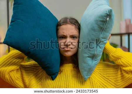 Repair work at neighbors. Irritated angry sad child girl kid cover ears with pillows annoyed by noisy loud music suffers headache wishes silence. Thin walls at home flat without sound insulation