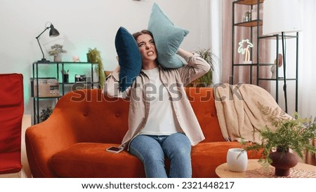 Repair work at neighbours. Irritated woman girl relaxing on couch cover ears with pillows annoyed by noisy neighbors suffer from headache wish silence. Thin walls at home flat without sound insulation