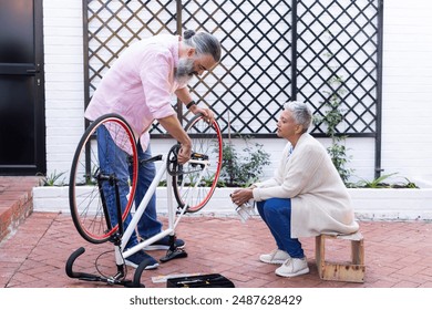 Repairing bicycle, senior man fixing bike while woman sitting and watching. Cycling, maintenance, teamwork, leisure, hobby, DIY - Powered by Shutterstock