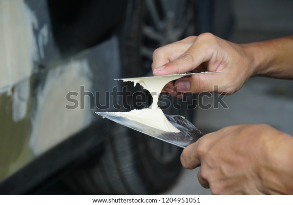 Repairing car body by puttying close up work\
after the accident by working sanding primer before painting. , The\
mechanic repair the car  , Using plastic putty ,Prepare surface for\
spray painting