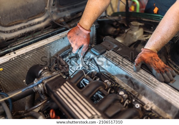 repairing a car engine in a car service, the hands\
of a mechanic unscrew the\
bolts