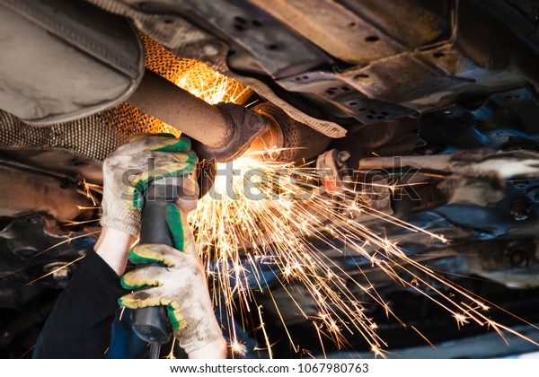 repairing of\
corrugation muffler of exhaust system in car workshop - repairer\
cuts old silencer on car by angle\
grinder