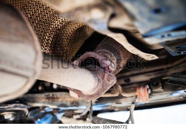 repairing of\
corrugation muffler of exhaust system in car workshop - bottom view\
of old broken muffler on\
car