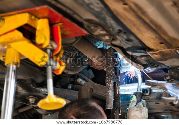 repairing of\
corrugation muffler of exhaust system in car workshop - worker\
welds the silencer on car by argon\
welding