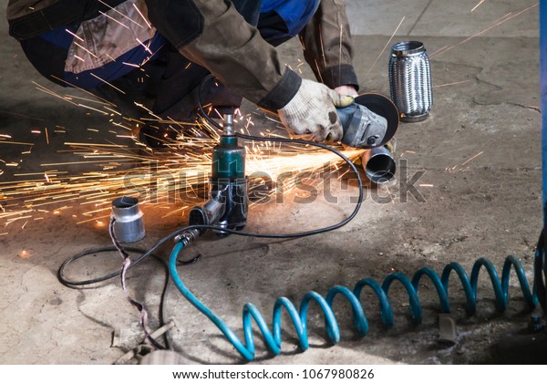 repairing of corrugation muffler of exhaust\
system in car workshop - mechanic cuts new pipe for corrugation\
silencer by angle\
grinder