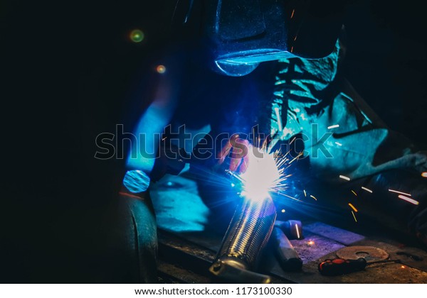 Repairing of corrugation muffler of exhaust\
system in car workshop - welder repairs the silencer on exhaust\
pipe by argon welding
