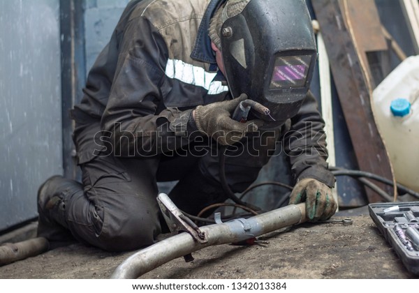 repairing of corrugation muffler of exhaust\
system in car workshop - serviceman welds the old silencer on car\
by argon welding
