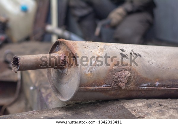 repairing of corrugation muffler of exhaust\
system in car workshop - serviceman welds the old silencer on car\
by argon welding