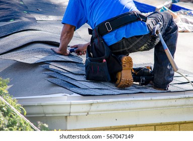 repairing the roof of a home; A worker replaces shingles on the roof of a home - Shutterstock ID 567047149